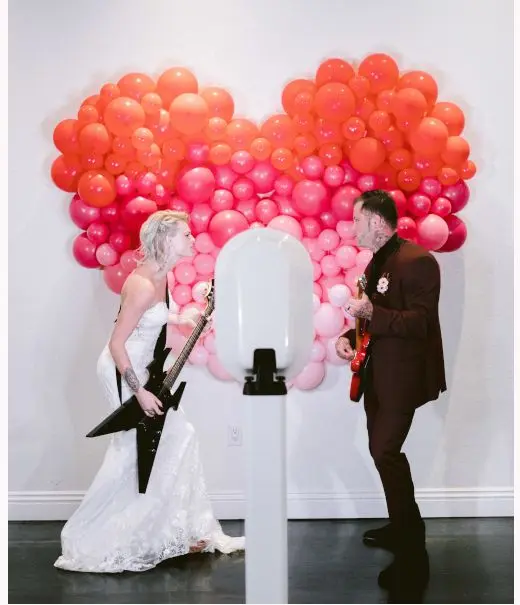 A bride and groom with guitars in front of a heart balloon wall